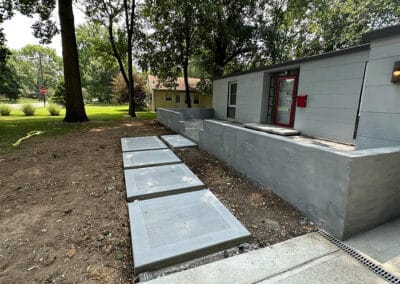Concrete pathway to home with concrete retaining wall, and stamped concrete front porch